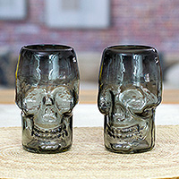 Handblown recycled glass tumblers, 'Smoke Mexican Skull' (pair) - 2 Black Clear Skull-Shaped Handblown Recycled Glass Tumblers